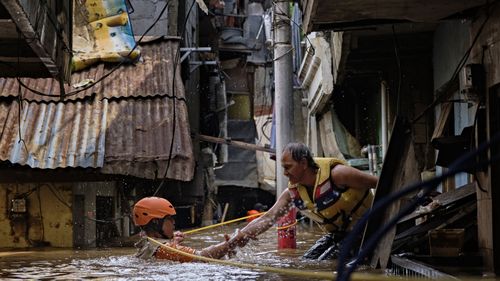 An Indonesian rescue worker helps his colleague as they navigate through a flooded neighbourhood on January 2, 2020 in Jakarta, Indonesia. 