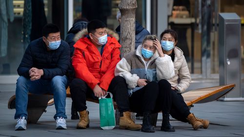 People wearing face masks to protect against COVID-19 sit on a bench at an outdoor shopping center in Beijing.