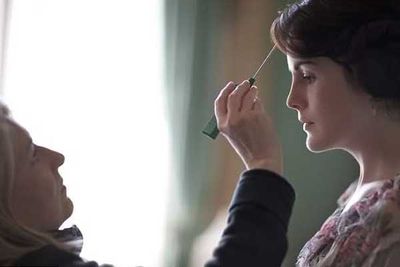 A stylist tends to stray hairs on Michelle Dockery (Lady Mary Crawley).