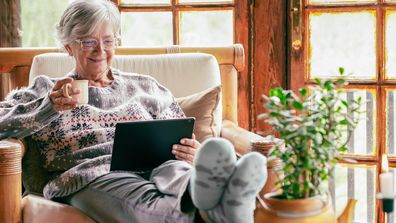 Senior citizen retiree old lady drinking coffee feet up reading ipad