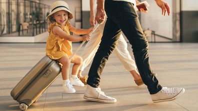 Cheerful husband and his anonymous wife walking with their little girl sitting on luggage at the airport.