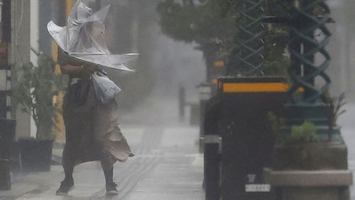 A woman makes her way through the strong wind and rain in Miyazaki, southern Japan, Sunday, Sept. 18, 2022, as a powerful typhoon pounded southern Japan. (Kyodo News via AP)