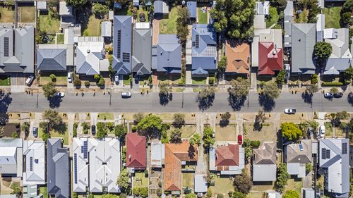 Vista aerea direttamente sopra le case consolidate nel vecchio sobborgo meridionale di Adelaide: guardando dall'alto sui cortili anteriori e posteriori, alcuni paesaggistici, uno con lavori di costruzione. I bidoni della spazzatura con ruote (spazzatura) con coperchio giallo e rosso sono parcheggiati sul marciapiede in attesa di raccolta. Le linee elettriche corrono lungo la strada verso le case. Auto parcheggiate in strada e in proprietà private.