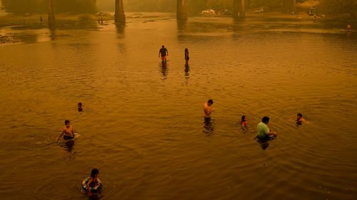 People wade in the river under a smoked-filled sky caused by wildfires, in Renaico Chile, Saturday, Feb. 4, 2023. Wildfires are spreading in southern and central Chile, triggering evacuations and the declaration of a state of emergency in some regions. 