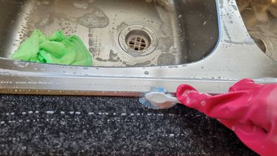 Cleaning the rim around the edge of the kitchen sink with a toothbrush