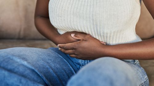 Cropped shot of a woman suffering from stomach pain on the sofa at home