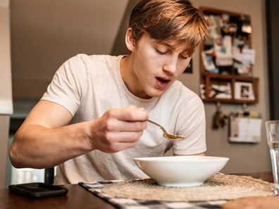 Stock image of a young man eating soup at home