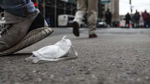 A used protective face mask rests on the pavement as pedestrians pass, Tuesday, March 17, 2020, in New York. 
