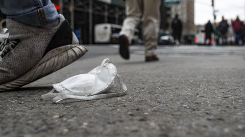 Un masque facial de protection usagé repose sur le trottoir au passage des piétons, mardi 17 mars 2020, à New York. 