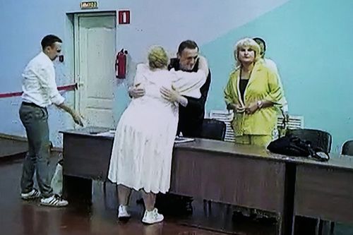 Russian opposition leader Alexei Navalny is seen on a TV screen embracing a lawyer, as he appears in a video link provided by the Russian Federal Penitentiary Service, during a hearing in the colony, in Melekhovo, Vladimir region, about 260 kilometres northeast of Moscow, Russia, on Friday, Aug. 4, 2023.  