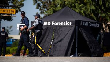 Police officers talk as a tent covers a body at the scene of a shooting in Langley, British Columbia.