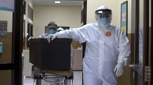 Health workers in protective suits carry a coffin containing the body of a COVID-19 victim for a burial in Denpasar, Bali, Indonesia.