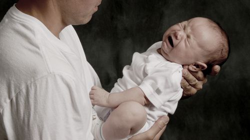 A father is holding his crying baby boy.
