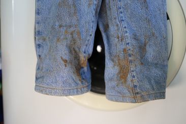Muddy jeans on a washing machine. Mud stain on jeans. Stained jeans before laundry.