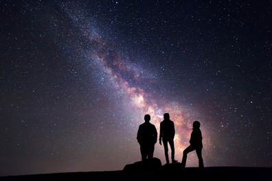 Milky Way. Night sky with stars and silhouette of a happy family with raised-up arms- istock