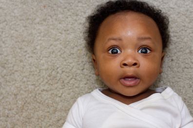 African American boy (6 months old) laying on his back looking up at the camera surprised with eyes open wide.