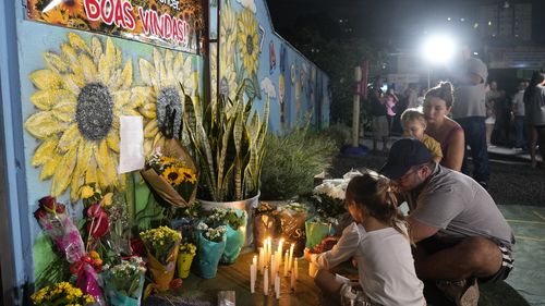 A family lights a candle at a makeshift memorial at the "Cantinho do Bom Pastor" daycare center after a fatal attack on children in Blumenau, Brazil, 