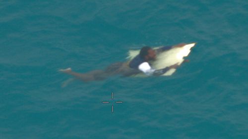 A man has survived clinging to a piece of debris for nearly 24 hours in shark and crocodile infested water in the Torres Strait after his boat was swamped by waves.