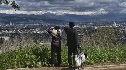 People take photos and view snow covering the San Gabriel mountain range from Kenneth Hahn State Recreational Area in Los Angeles on Sunday, Feb. 26, 2023. 