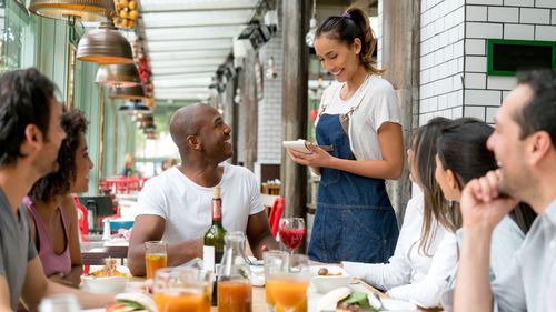 Happy waitress taking orders to a group of people eating together at a restaurant