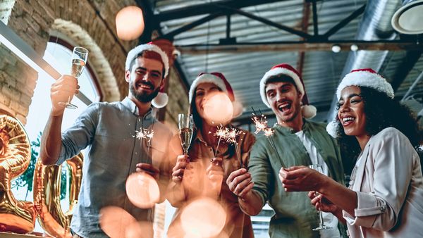 Young creative team with sparklers and Santa hats celebrating the holidays in a modern office. 