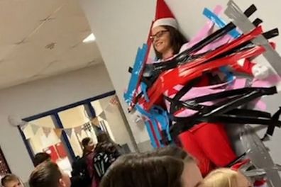 Beth Hoeing dressed as an elf while being tapped to the wall.