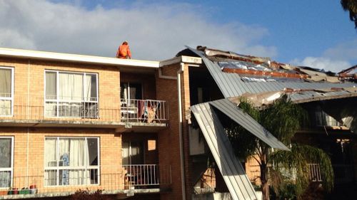 An SES worker examines the damage after the roof of an apartment in Attadale blew off in last night's wild weather. (9NEWS)