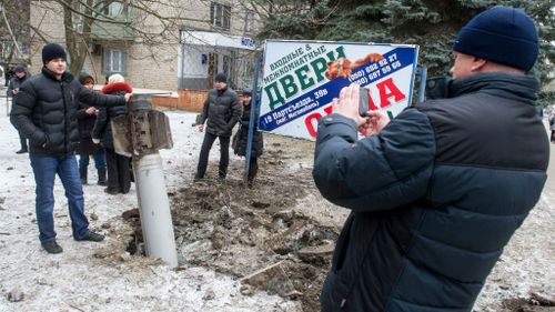 A man poses for a photograph beside an unexploded rocket embedded in the street after shelling in eastern Ukrainian city of Kramotorsk. (Getty)