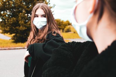 Two Teenage Girls doing an Elbow Bump to greet each other meeting outside during Covid-19 pandemic times. Wearing surgical face masks greeting each other securely with an elbow bump. Avoiding tight body contact, handshakes and huggings with the new elbow bump greeting procedure. Covid-19 Pandemic Times Youth Culture Lifestyle..