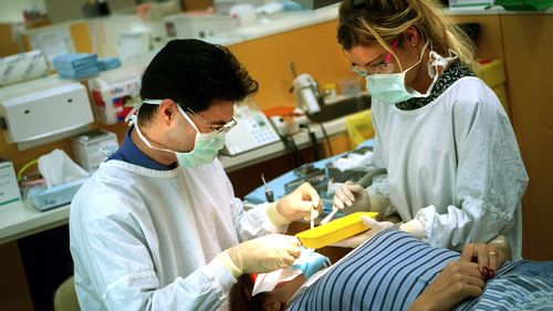 A dentist and his assistant carry out procedures on a patient.