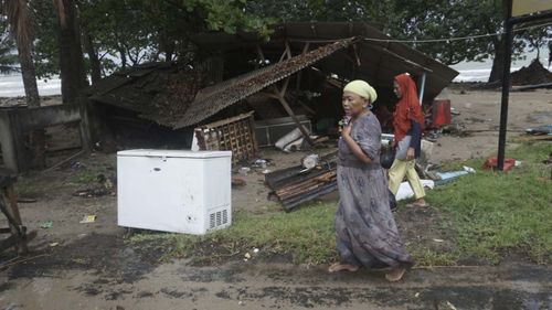 Residents walk past a house damaged by a tsunami, in Carita, Indonesia.