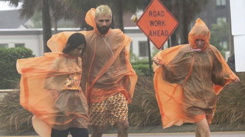 People in raincoats walk along International Drive in Orlando, Fla., Wednesday, Sept. 28, 2022, as the first effects of Hurricane Ian are felt in central Florida. (Joe Burbank/Orlando Sentinel via AP)