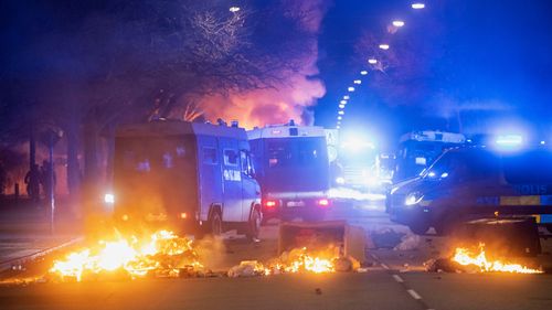 Police on buses try to break up the crowd as a city bus burns on a street in Malmo, Sweden.
