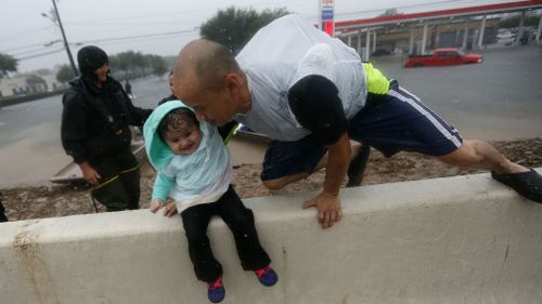 Vinh Nguyen rests his daughter Kailie, 18 months, as he hops over a highway divider after being rescued in boats by the Louisiana Department of Wildlife and Fisheries. (AAP)