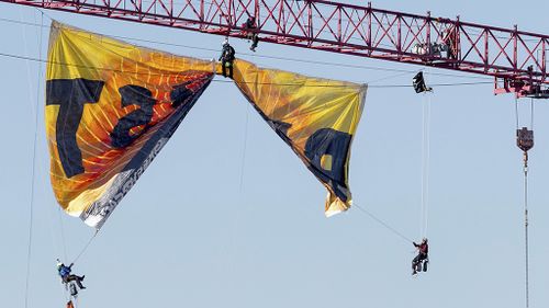 Protesters chained themselves to the crane while others attached to wires unfurled the banner. (AAP)