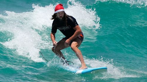 A surfer wearing a Santa hat as he catches a wave