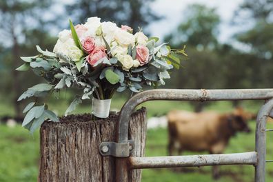 Wedding flowers sitting on fence gate post in rural scene.