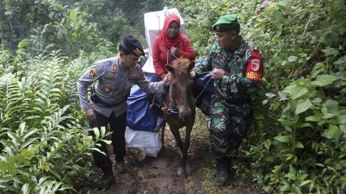 A police officer and a soldier assist a worker as they use horses to distribute ballot boxes and other election paraphernalia to polling stations in remote villages in Tempurejo, East Java, Indonesia.
