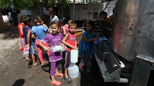 Palestinian children sheltering in a UN school in Gaza line up for water. (Getty)