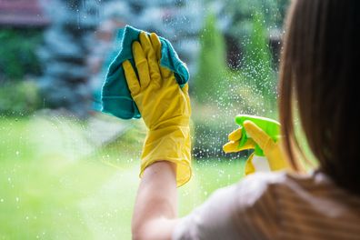 Unrecognisable woman cleaning windows of country house
