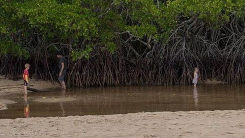 Man turns his back as young girl wades near crocodile-infested creek