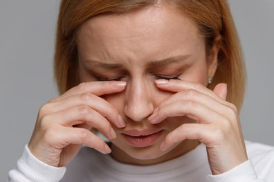 Close up of young woman has a problem with contact lenses, rubbing her swollen eyes due to pollen, dust allergy. Dry eye syndrome, watery, itching. Isolated on grey background