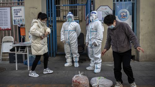 An epidemic control worker and a security guard wear protective suits to prevent the spread of COVID-19 as a resident collects a food order outside an apartment building in the Central Business District on November 26, 2022 in Beijing, China. 
