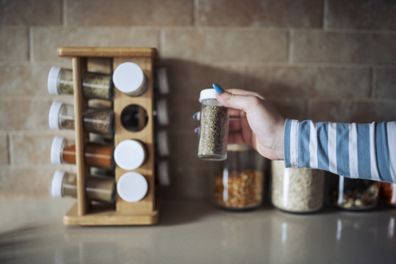 Cropped hand holding jar of spices on kitchen counter.