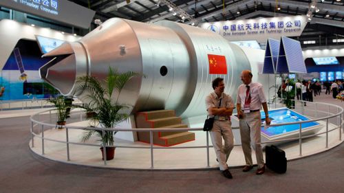 Visitors sit beside a model of China's Tiangong-1 space station at the 8th China International Aviation and Aerospace Exhibition in Zhuhai in 2010. (AP)