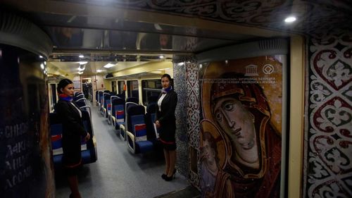 rain hostesses stand in a train carriage decorated with iconic religious figures as it departs from Belgrade to Mitrovica, Kosovo.