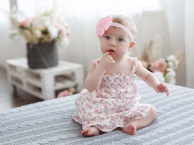 Baby girl wearing a pink dress sitting on a bed.