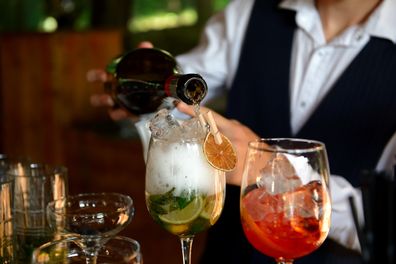 Champagne cocktail. The bartender pours champagne into a glass to prepare a fashionable cocktail. Close-up with people's hands.