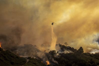 Water is dropped on the advancing Palisades Fire by helicopter in the Pacific Palisades neighborhood of Los Angeles, Tuesday, Jan. 7, 2025. (AP Photo/Ethan Swope)