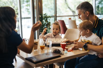 Young family, husband, wife and two kids, son and daughter enjoying drink and time together at restaurant, looking at menu and preparing to order the food